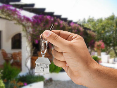 A hand holding a key with silver house pendant for key holding service with holidayhome in the back